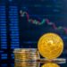 Close-up of golden Bitcoins on a dark reflective surface and the histogram of decreasing crypto in the background