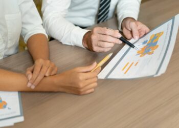 Close-up of multiethnic managers discussing international sales while analyzing data. Unrecognizable analysts viewing map while working with statistics. Forecasting concept