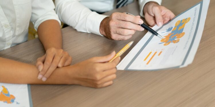 Close-up of multiethnic managers discussing international sales while analyzing data. Unrecognizable analysts viewing map while working with statistics. Forecasting concept