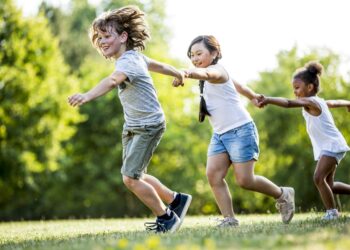 Children holding hands and running in park, smiling.