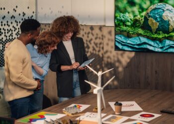 Smiling multicultural businesspeople standing at minimalistic office with tablet in hands and working on pollution reduction technology. Diverse staff collaborating on renewable energy technology.