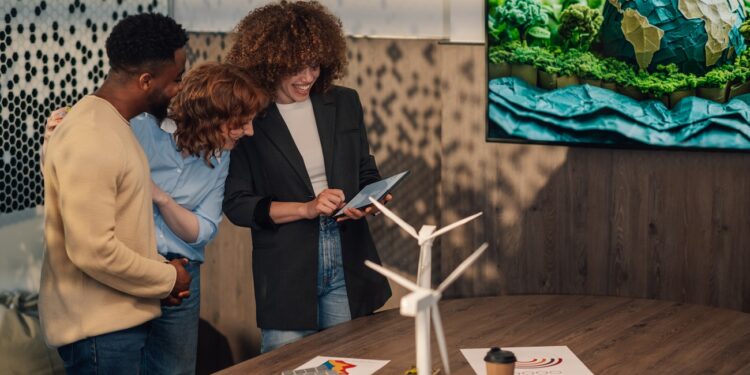 Smiling multicultural businesspeople standing at minimalistic office with tablet in hands and working on pollution reduction technology. Diverse staff collaborating on renewable energy technology.