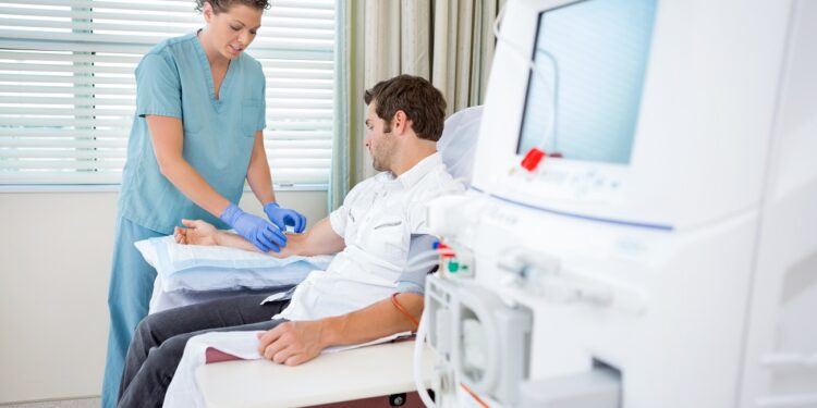 Mid adult female nurse injecting patient for renal dialysis treatment in hospital room