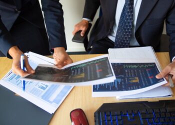 Investor and trader discussing statistic data, holding papers with financial charts and pen. Cropped shot. Broker job or trading concept