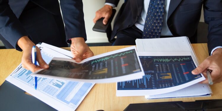 Investor and trader discussing statistic data, holding papers with financial charts and pen. Cropped shot. Broker job or trading concept
