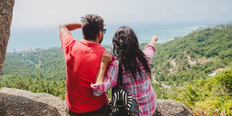 young happy hipster couple in love traveling around world, sightseeing, tropical romantic vacation in thailand, sitting on a rock, pointing finger, active tourism, summer