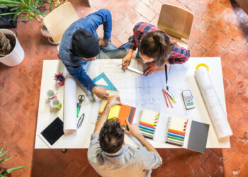 three young architects are having a meeting at a table office studiyng a plan and discussing on a colour chart