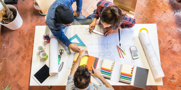 three young architects are having a meeting at a table office studiyng a plan and discussing on a colour chart