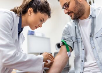 Friendly hospital phlebotomist collecting blood sample from patient in lab. Preparation for blood test by female doctor medical uniform on the table in white bright room