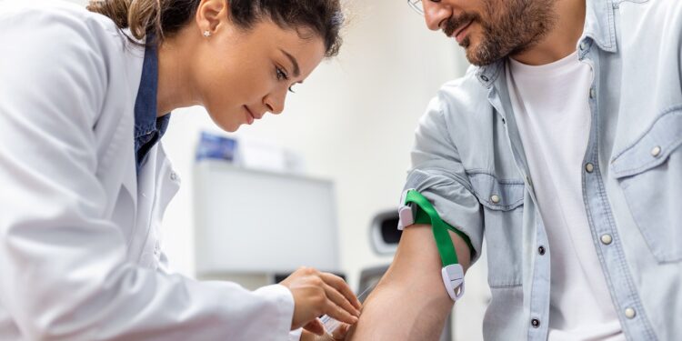 Friendly hospital phlebotomist collecting blood sample from patient in lab. Preparation for blood test by female doctor medical uniform on the table in white bright room