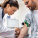 Friendly hospital phlebotomist collecting blood sample from patient in lab. Preparation for blood test by female doctor medical uniform on the table in white bright room