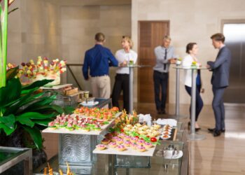 View of different canapes, tartlets and snacks on buffet table in restaurant. Business people eating and talking in background. Catering concept