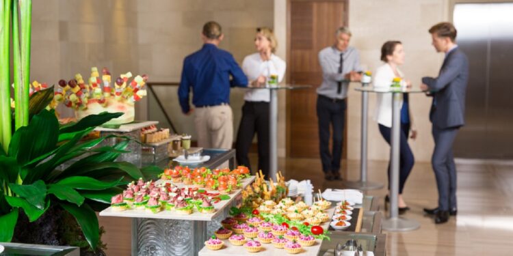 View of different canapes, tartlets and snacks on buffet table in restaurant. Business people eating and talking in background. Catering concept