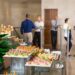 View of different canapes, tartlets and snacks on buffet table in restaurant. Business people eating and talking in background. Catering concept