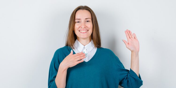 young woman keeping hand on chest, showing palm in sweater over white shirt and looking merry. front view.