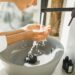 Spa treatment. Bathroom with white walls full of sun light. Black metal furniture. Grey stone sink. Person in bathrobe. Trendy interior design
