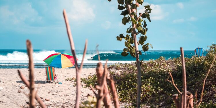 A beautiful shot of a beach with a colorful parasol and a beach chair with amazing waves on a sunny day