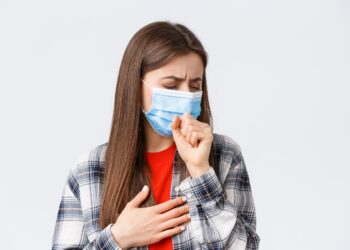 Coronavirus outbreak, leisure on quarantine, social distancing and emotions concept. Close-up of sick young woman in medical mask staying at home during covid-19, cough with closed eyes.
