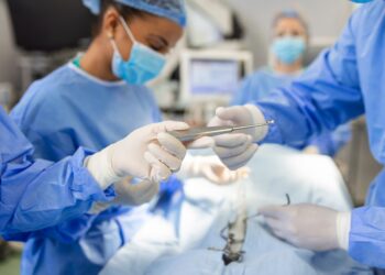 Low Angle Shot in the Operating Room, Assistant Hands out Instruments to Surgeons During Operation. Surgeons Perform Operation. Professional Medical Doctors Performing Surgery.