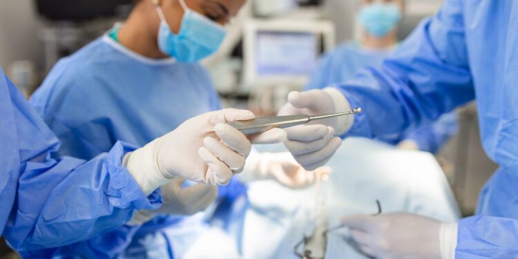 Low Angle Shot in the Operating Room, Assistant Hands out Instruments to Surgeons During Operation. Surgeons Perform Operation. Professional Medical Doctors Performing Surgery.