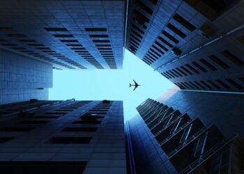 Digital generated image of buildings making arrow sign with airplane flying on blue sky.