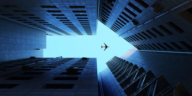 Digital generated image of buildings making arrow sign with airplane flying on blue sky.
