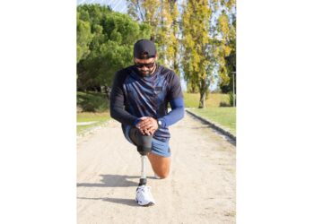 Sporty man with artificial leg getting ready for jog. Man in sport clothes stretching legs in park on summer day. Sport, training, wellbeing concept
