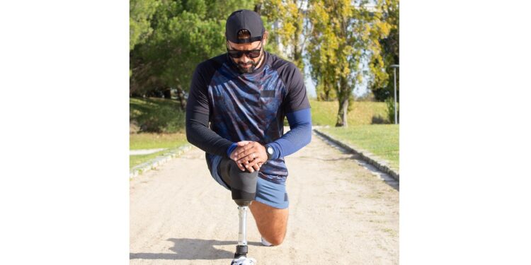 Sporty man with artificial leg getting ready for jog. Man in sport clothes stretching legs in park on summer day. Sport, training, wellbeing concept