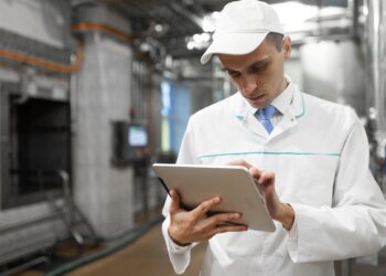 technologist with grey tablet in his hands make a set up of the production line while standing at the department of dairy factory