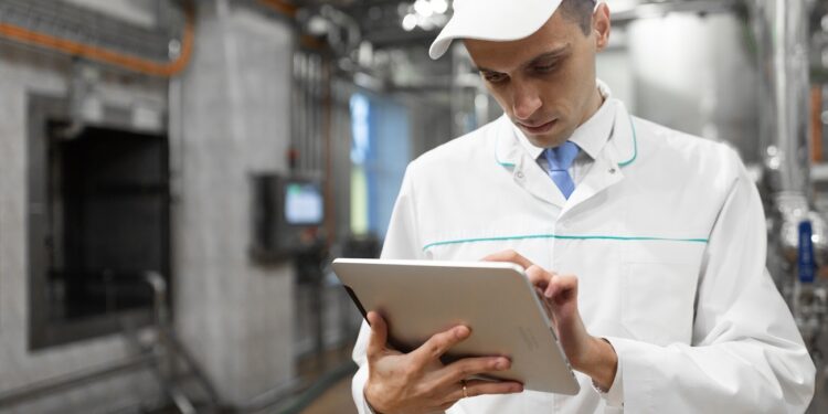technologist with grey tablet in his hands make a set up of the production line while standing at the department of dairy factory