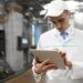 technologist with grey tablet in his hands make a set up of the production line while standing at the department of dairy factory
