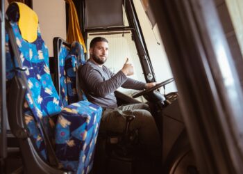 A bus driver posing for a photo in a bus with a smile and thumb up.