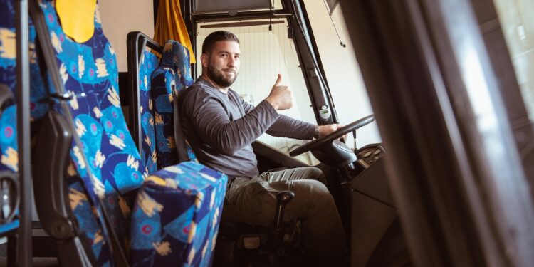 A bus driver posing for a photo in a bus with a smile and thumb up.