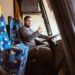 A bus driver posing for a photo in a bus with a smile and thumb up.