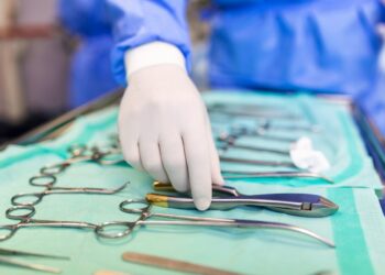 Surgeon picking up surgical tool from tray. Surgeon is preparing for surgery in operating room. He is in a hospital.