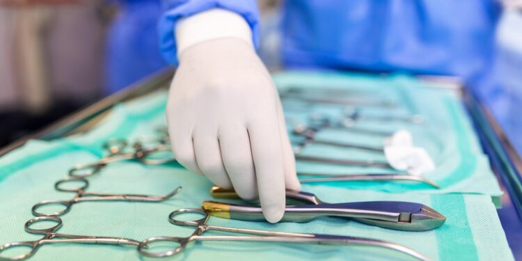 Surgeon picking up surgical tool from tray. Surgeon is preparing for surgery in operating room. He is in a hospital.