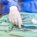Surgeon picking up surgical tool from tray. Surgeon is preparing for surgery in operating room. He is in a hospital.