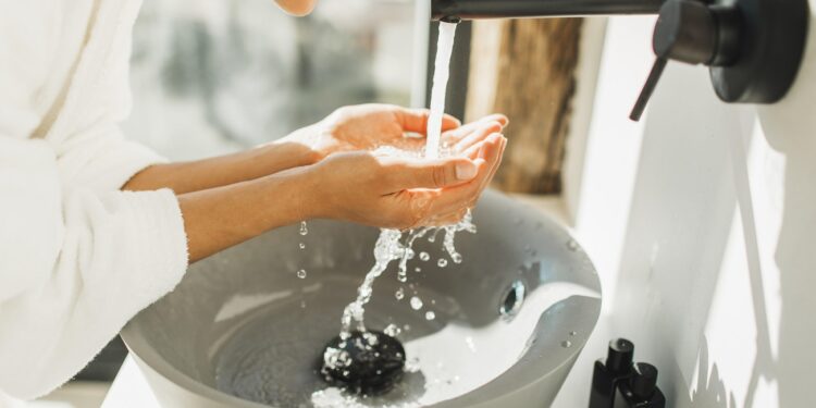 Spa treatment. Bathroom with white walls full of sun light. Black metal furniture. Grey stone sink. Person in bathrobe. Trendy interior design