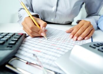 Photo of human hands holding pencil and ticking data in documents