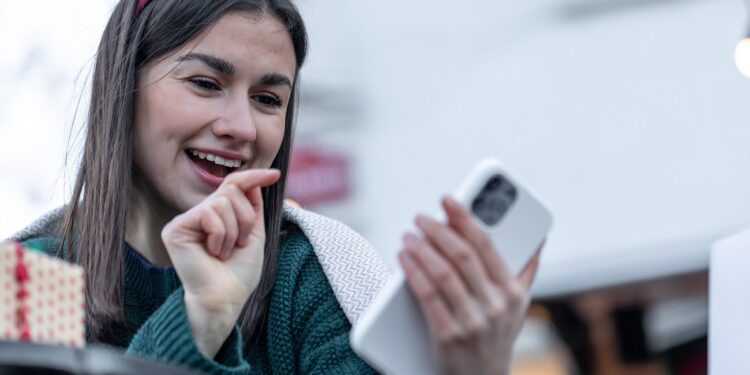 Stylish young woman on a walk in the city holding a smartphone in her hands, Christmas stylish look.