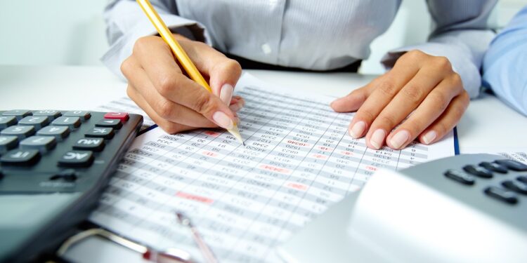 Photo of human hands holding pencil and ticking data in documents