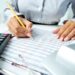 Photo of human hands holding pencil and ticking data in documents