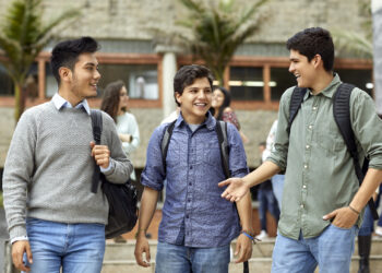 Smiling young men talking while walking in campus. Happy male students are listening to friend. They are in casuals.