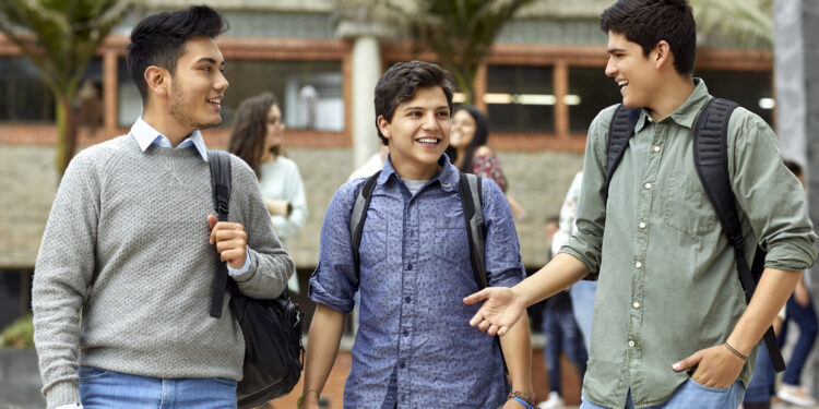 Smiling young men talking while walking in campus. Happy male students are listening to friend. They are in casuals.
