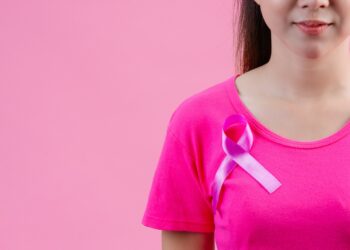 Breast cancer awareness month, Woman in pink t-shirt with satin pink ribbon on her chest, supporting symbol of breast cancer awareness campaign in October.