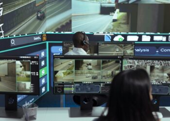 African american employee following delivery trucks around the city, sending gps coordinates for cargo location by using satellite map. Monitoring couriers in traffic on CCTV footage.
