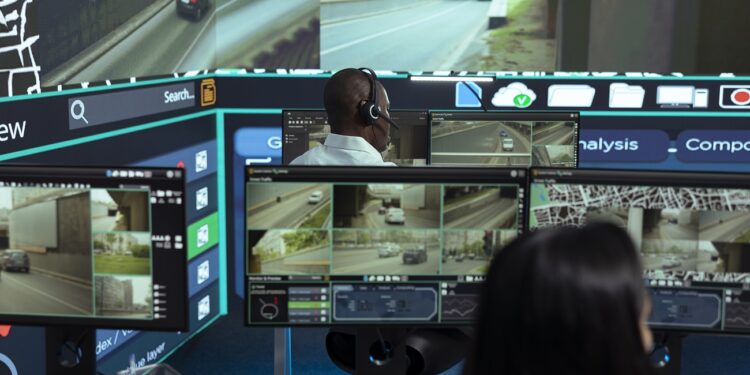 African american employee following delivery trucks around the city, sending gps coordinates for cargo location by using satellite map. Monitoring couriers in traffic on CCTV footage.