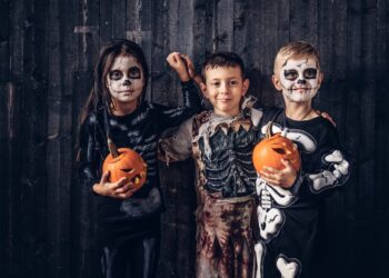 Three multiracial kids in scary costumes posing with pumpkins in an old house. Halloween concept.