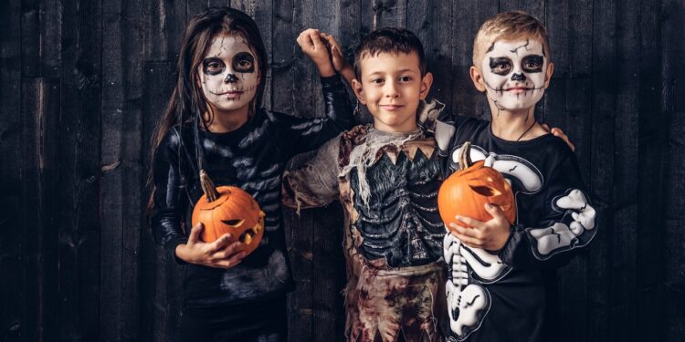 Three multiracial kids in scary costumes posing with pumpkins in an old house. Halloween concept.