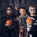 Three multiracial kids in scary costumes posing with pumpkins in an old house. Halloween concept.